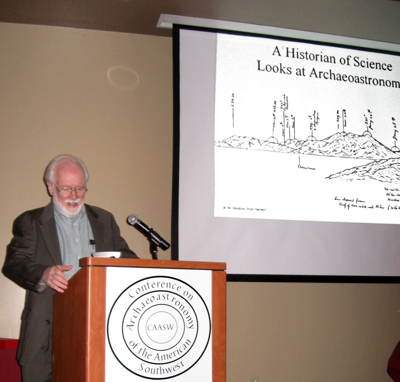 Stephen McCluskey speaking at a CAASW lectern in front of a projected slide titled “A Historian of Science Looks at Archaeoastronomy”