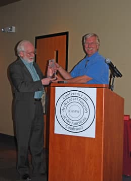 Dr. Stephen McCluskey receives a glass award from Dr. Todd Bostwick at a CAASW podium