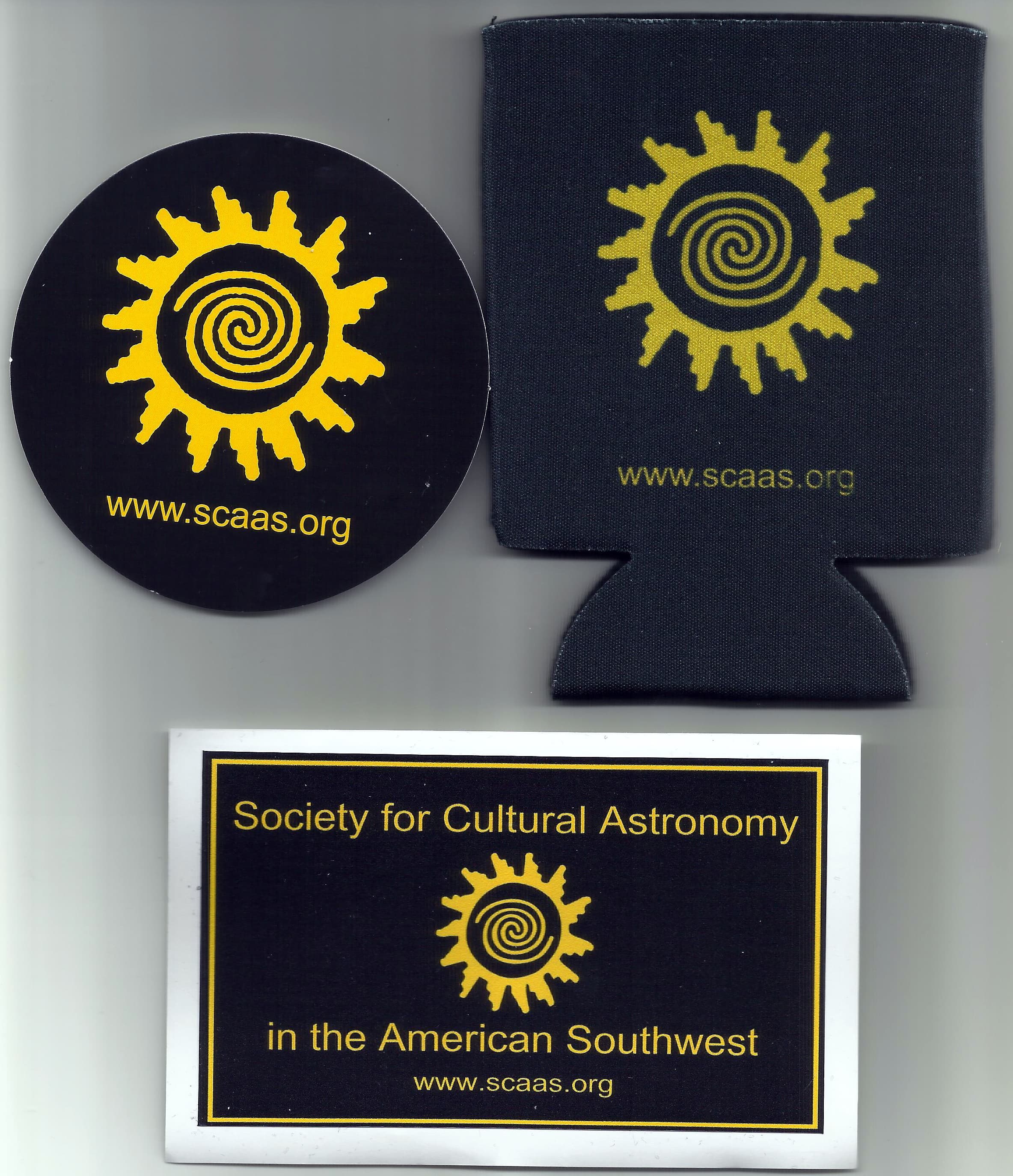 The SCAAS Gift Set: a round black sticker and a black can koozie, both with the gold spiral sun and www.scaas.org, and a black and gold Society for Cultural Astronomy in the American Southwest decal