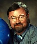 Dr. Michael Zeilik, with glasses, beard and tie, beside a blue celestial globe